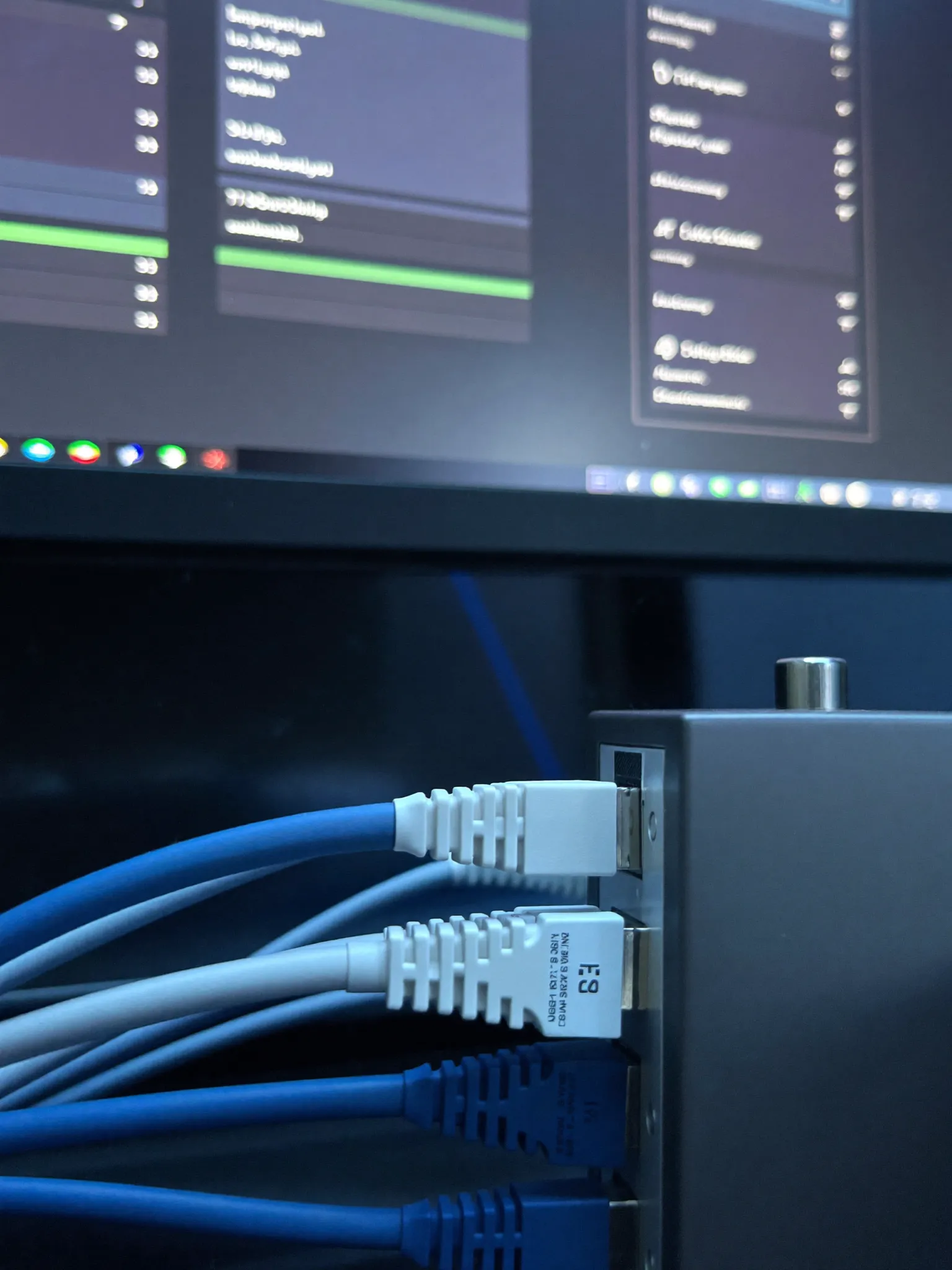 Neatly bundled network cables plugged into a switch, with a monitor showing a clean systems dashboard behind in cool blue light